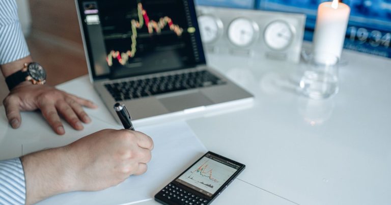 Beyaz masada dizüstü bilgisayar ve grafik gösteren telefonla not alan analist