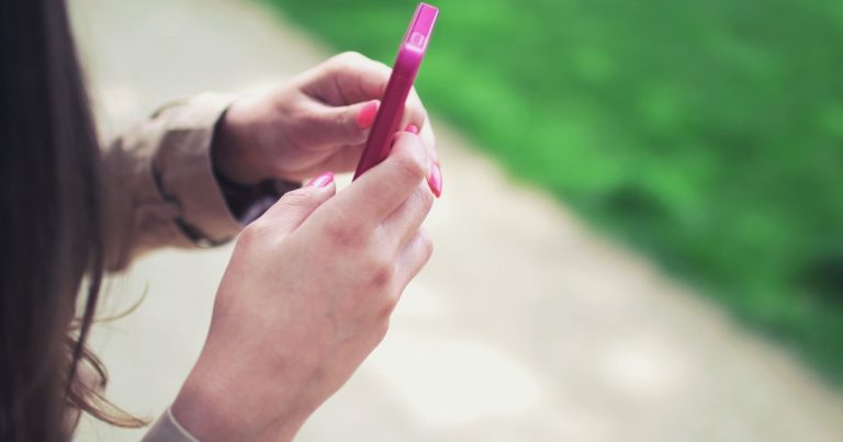 Dış mekânda pembe telefonu iki eliyle tutan kadın