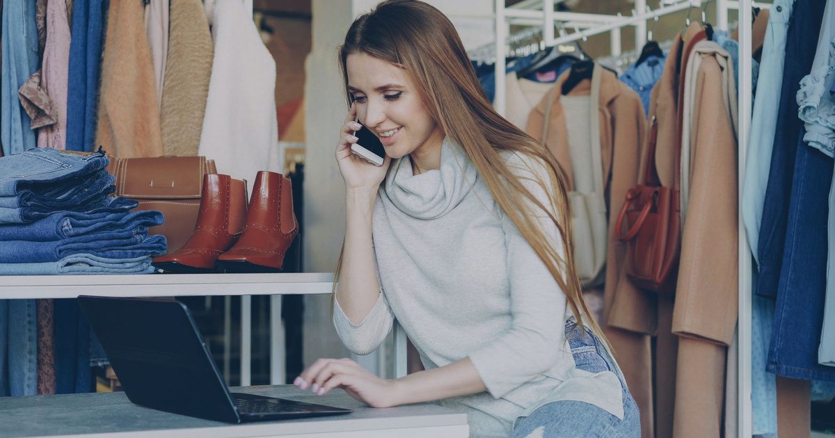 Butiğinde dizüstü bilgisayar ve telefon kullanan güler yüzlü kadın