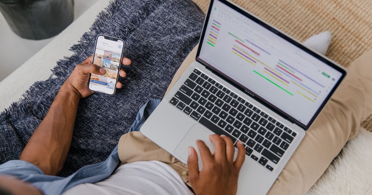 Kanepede telefon ve dizüstü bilgisayarı birlikte kullanan adam