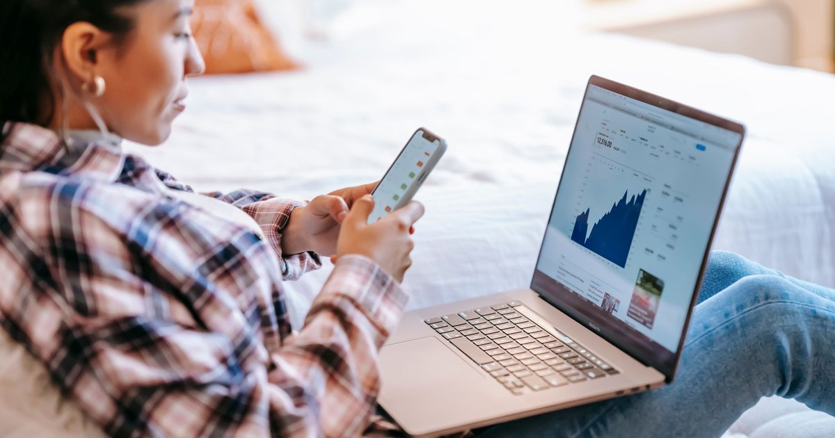 Dizüstü bilgisayar önünde telefonda grafik uygulaması kullanan kadın