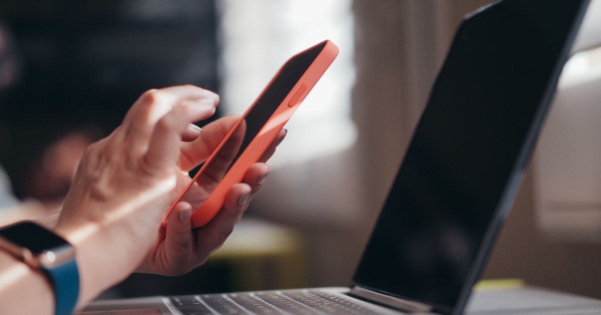 İç mekânda telefon ve dizüstü bilgisayarı birlikte kullanan kişi