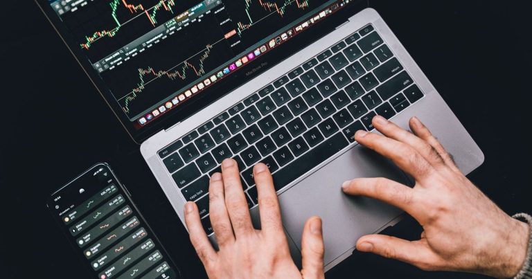 Telefon yanında grafik ekranı açık dizüstü bilgisayarda yazı yazan eller