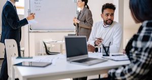 Dizüstü bilgisayarlar ve beyaz tahtayla toplantı yapan profesyoneller