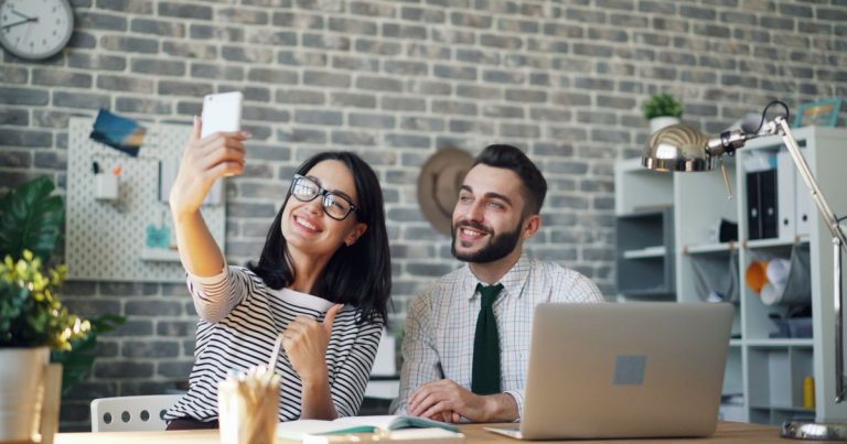 Çalışma alanında telefonla özçekim yapan güler yüzlü çalışma arkadaşları