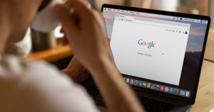 Kahvesini içerken dizüstü bilgisayarda Google'da arama yapan kişi