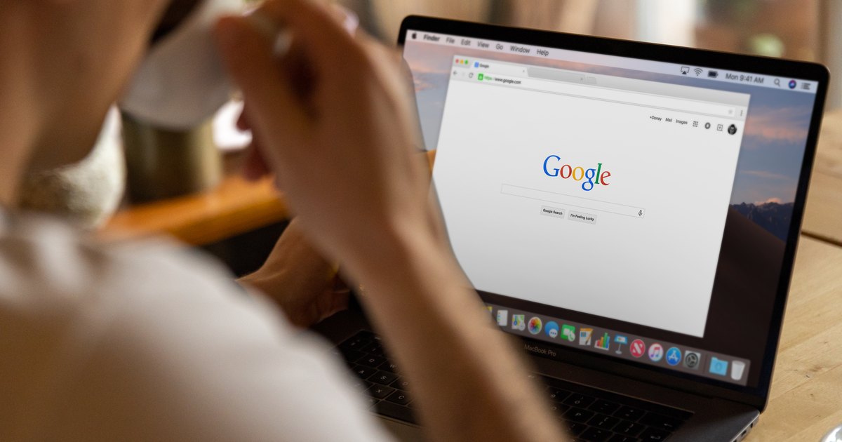 Kahvesini içerken dizüstü bilgisayarda Google'da arama yapan kişi
