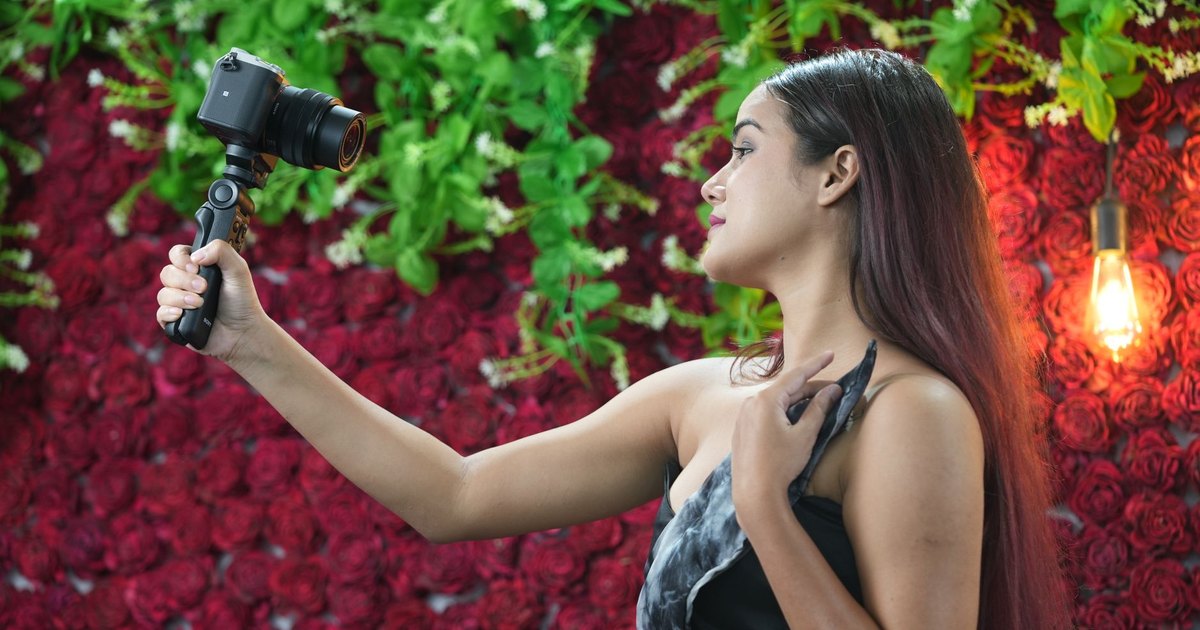 Çiçekli bir fonun önünde kamerayla fotoğraf çeken kadın
