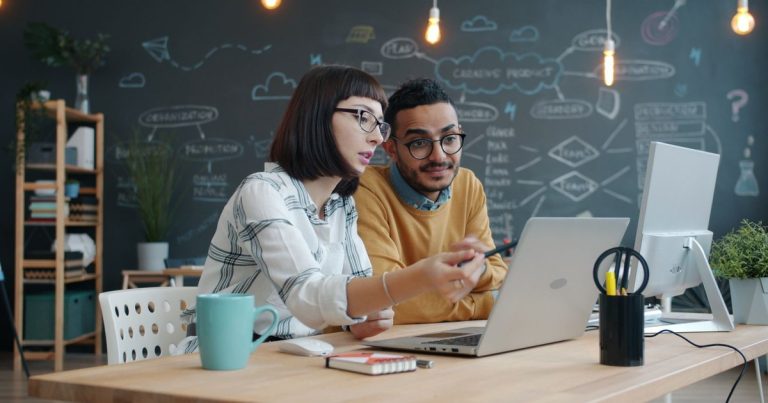 Modern ofiste bir proje üzerinde birlikte çalışan iki çalışma arkadaşı