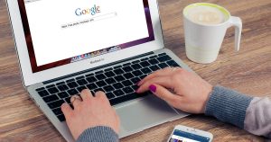Kahve yanında Google arama sayfası açık dizüstü bilgisayarda yazı yazan eller