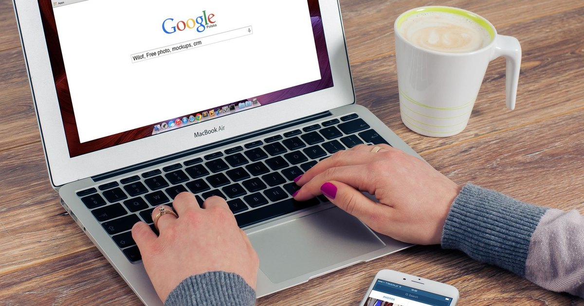 Kahve yanında Google arama sayfası açık dizüstü bilgisayarda yazı yazan eller