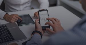 Masada akıllı telefonda reklam grafiği inceleyen iki iş insanı, yanında tablet ve dizüstü bilgisayar