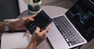 Modern çalışma alanında dizüstü bilgisayar ve telefonda grafik inceleyen adam