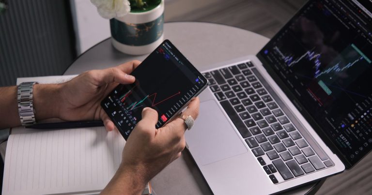 Modern çalışma alanında dizüstü bilgisayar ve telefonda grafik inceleyen adam