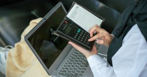Laptop başında hesap makinesiyle reklam maliyeti hesaplayan kişi