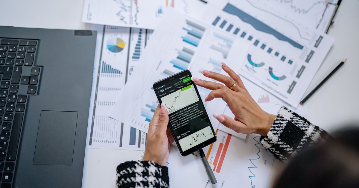 Dizüstü bilgisayar ve belgelerin yanında telefonda grafik inceleyen iş kadını