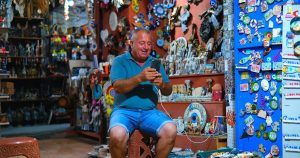 Rengarenk hediyelik eşya dükkânında telefonunu kullanan güler yüzlü esnaf